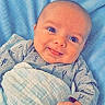 baby, infant, child, smiling, tongue_out, portrait, close_up, lying_down, blanket, bedding, blue, indoor, face, eyes, hand, onesie, clothing, cozy, happy, photography