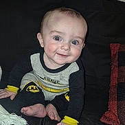 Emerson is registered to the contest to win money with this photo: baby, child, infant, smiling, happy, portrait, sitting, couch, sofa, blanket, throw, batman, superhero, costume, clothing, black_and_yellow, blue_eyes, indoor, living_room, adorable