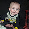 baby, child, infant, smiling, happy, portrait, sitting, couch, sofa, blanket, throw, batman, superhero, costume, clothing, black_and_yellow, blue_eyes, indoor, living_room, adorable