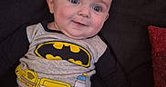 Emerson joined the competition — help win amazing prizes! baby, child, infant, portrait, smiling, happy, sitting, couch, sofa, batman, superhero, costume, clothing, gray_outfit, black, yellow, red_cushion, indoor, home, face