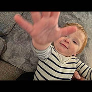 Riley is registered to the contest to win money with this photo: blanket, casual_clothing, child, couch, face, hair, hand, happy, head, home, indoor, person, playful, portrait, reaching, skin, smile, striped_shirt, toddler, young