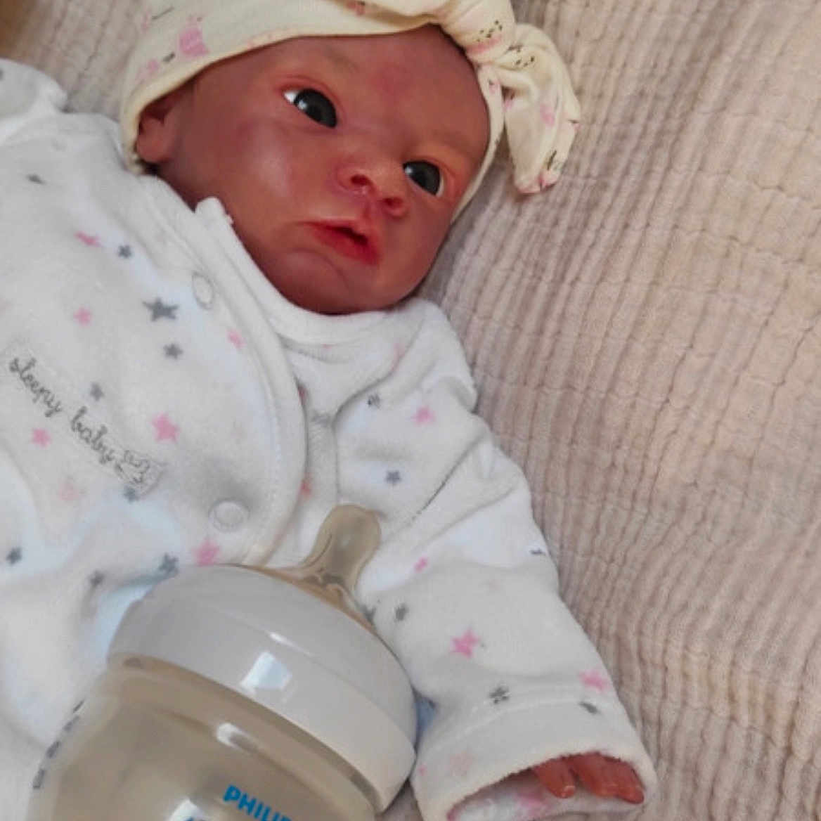 Sallomé participe au concours pour gagner de l'argent avec cette photo : baby_bottle, baby_doll, blanket, bow, clothing, face, hand, headband, infant, lying_down, newborn, onesie, philips_avent, pink, realistic, soft, star_pattern, texture, toy, white