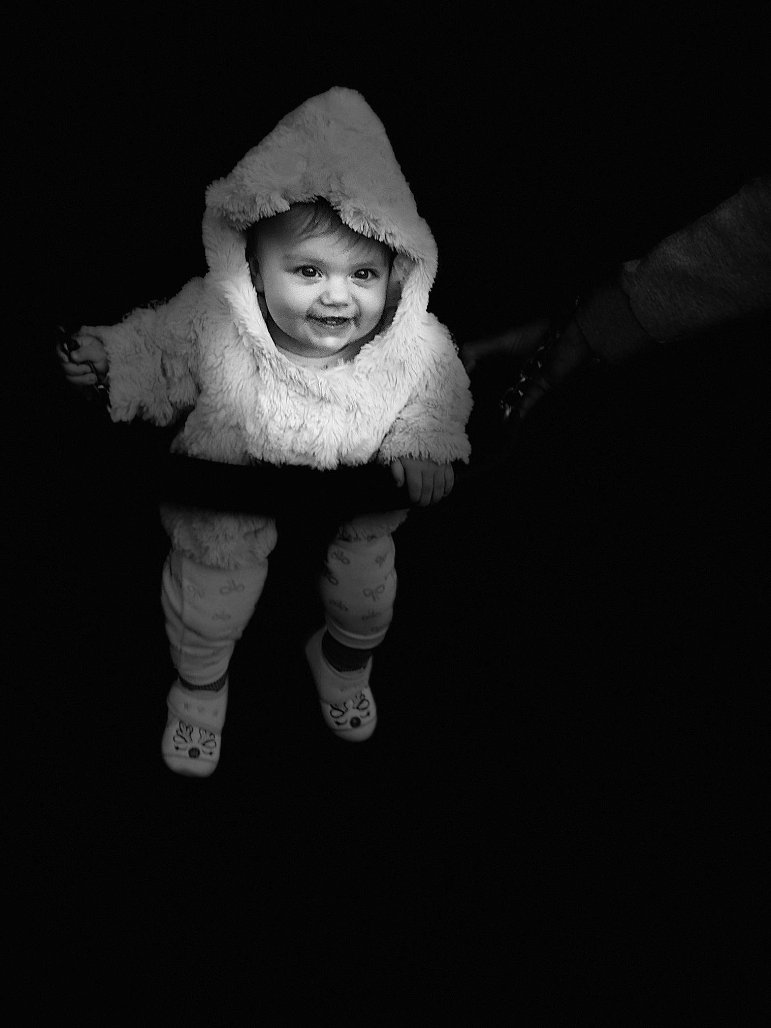 Siana participe au concours pour gagner de l'argent avec cette photo : baby, baby_toddler_clothing, child, darkness, flash_photography, foot, fun, fur, gesture, happy, headwear, joy, monochrome, monochrome_photography, person, portrait, portrait_photography, sitting, sleeve, smile
