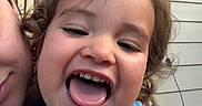 Asiah joined the competition — help win amazing prizes! adult_partial, blue_shirt, casual, child, closeup, curly_hair, daylight, expression, face, fun, happy, joy, outdoor, person, porch, portrait, smiling, string_lights, toddler, tongue_out