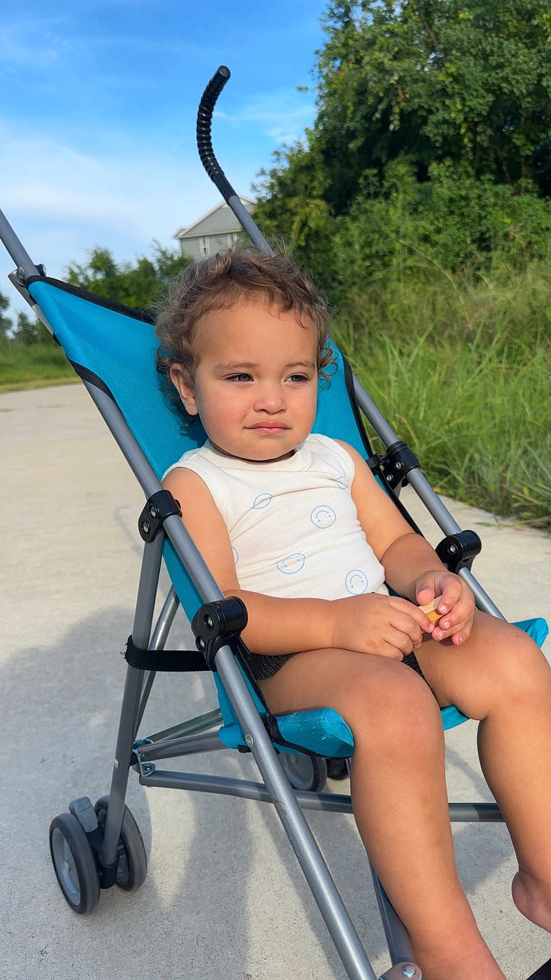 Asiah joined the competition — help win amazing prizes! child, stroller, outdoor, sunlight, curly_hair, blue, greenery, sidewalk, thoughtful, person, summer, casual_clothing, baby, nature, daytime, sitting, expression, small_object, wheels, relaxing