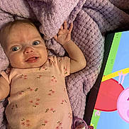 Laynna is registered to the contest to win money with this photo: baby, cartoon, child, childrens_toy, close_up, face, floral_pattern, hand, happy, indoors, infant, lying_down, pacifier, pink_onesie, portrait, purple_blanket, skin, smiling, tablet, technology