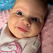 Selena is registered to the contest to win money with this photo: baby, smiling, face, close_up, blanket, pink, soft_texture, cute, infant, portrait, child, sleepwear, cozy, indoors, eyelashes, expression, head, clothing, fabric, young