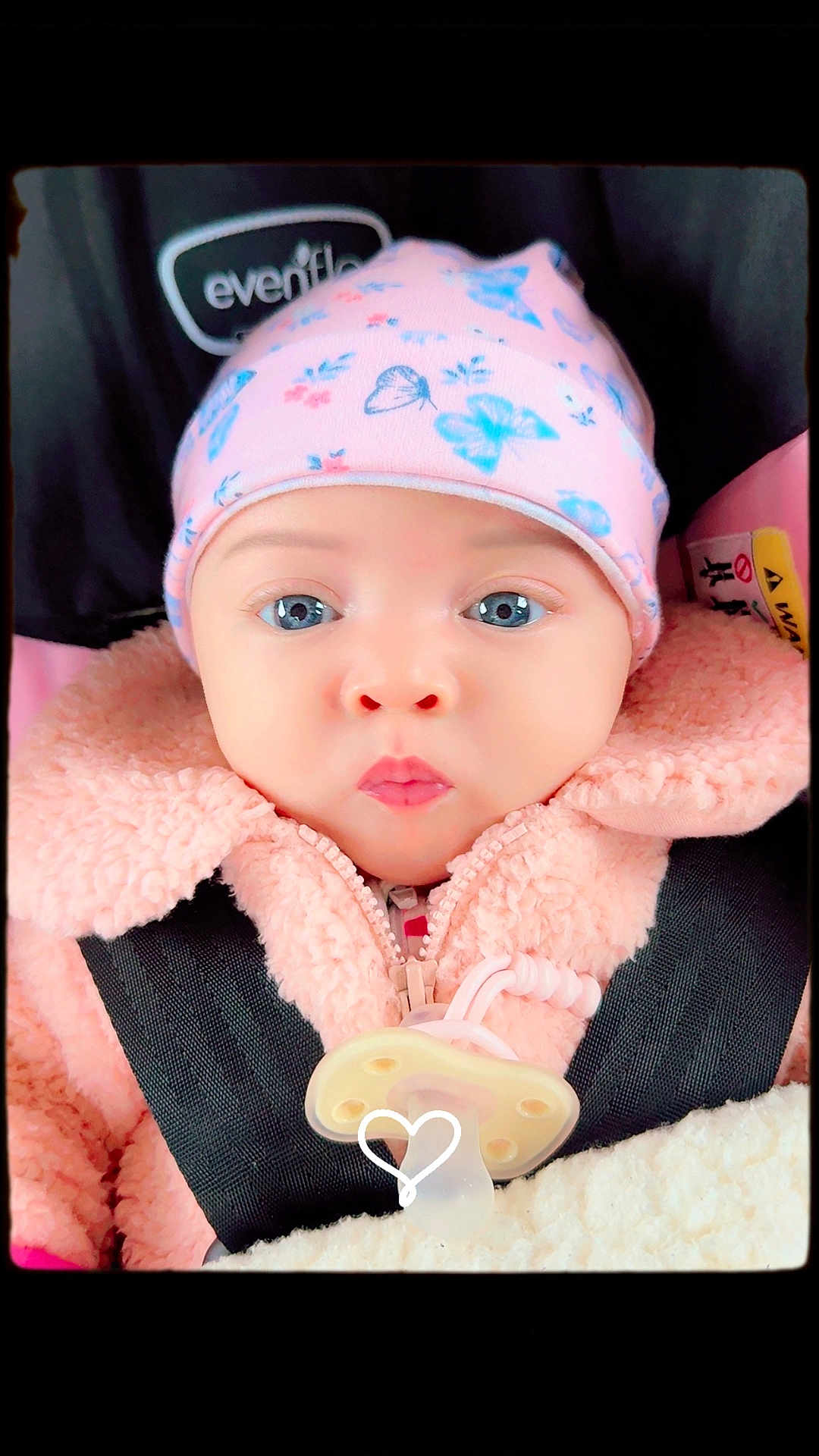 Kaiiv is registered to the contest to win money with this photo: baby, infant, car_seat, hat, pink_clothing, pacifier, blanket, face, blue_eyes, jacket, child, cute, portrait, closeup, winter_clothing, straps, seatbelt, expression, indoors, person