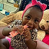 baby, child, girl, headband, bow, leopard_print, pink_clothing, teddy_bear, bed, cuddly_toy, smiling, chewing, indoor, cozy, furniture, mirror, bottle, person, happy, cute