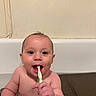 baby, bathroom, bathtub, child, cleaning, cute, face, hand, hygiene, indoors, mouth, person, playful, red_cup, sitting, skin, smiling, toothbrush, water, young_child