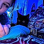 person, cat, black_cat, bed, blanket, bedding, nail_art, hand, indoor, blue_light, decor, pillow, face, fur, eye, bedroom, cozy, pattern, gesture, portrait