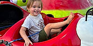 Rae joined the competition — help win amazing prizes! child, toddler, smiling, amusement_park, ride, ladybug, red, green, shorts, tshirt, happy, outdoor, daylight, people, fence, superhero_mural, background, fun, playful, leisure