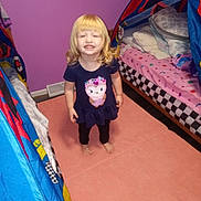 Khloe is registered to the contest to win money with this photo: child, smiling, barefoot, pink_carpet, bedroom, bed, tent, pillow, purple_wall, navy_blue_dress, owl_design, young_child, indoor, carpet, furniture, person, room, happy, curly_hair, playful
