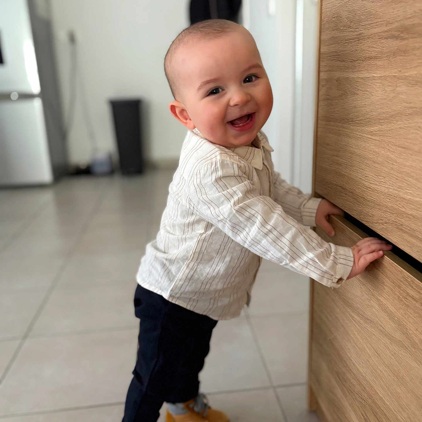 Vittorio participe au concours pour gagner de l'argent avec cette photo : baby, boots, eyes, face, floor_tiles, furniture, hands, happy, home_interior, kitchen, pants, portrait, refrigerator, smiling, standing, striped_shirt, tile_floor, toddler, trash_bin, wooden_drawer