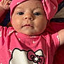 baby, infant, pink_clothing, headband, bow, hello_kitty, face, eyes, mouth, hand, quilt, fabric, pattern, cute, child, portrait, laying_down, indoors, skin, apparel
