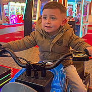 Timeo a rejoint le concours — aidez-le/la à gagner de superbes lots ! child, boy, arcade, motorcycle_ride, indoor, game_machine, neon_lights, playful, jacket, pants, sneakers, entertainment, fun, amusement, colorful, young, smiling, hands_on_handlebars, floor, lighting