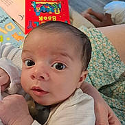 Ace joined the competition — help win amazing prizes! baby, infant, face, hand, person, clothing, pacifier, book, background, floor, skin, eyes, curious, holding, sitting, home, indoor, child, cute, young