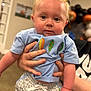 Kingston is registered to the contest to win money with this photo: baby, child, party_hat, blue_shirt, fish_embroidery, checkered_pants, hand, person, indoor, celebration, balloons, blurred_background, cute, chubby_cheeks, young_child, portrait, holding, smiling, eyes, infant