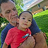 child, adult, man, toddler, outdoor, grass, house, sky, trees, greenery, tattoo, red_shirt, blue_shirt, holding, portrait, family, daylight, nature, affection, casual_clothing