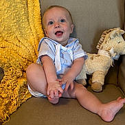 Saban is registered to the contest to win money with this photo: baby, child, smiling, blue_outfit, couch, blanket, plush_toy, stuffed_animal, happy, indoor, cute, sitting, infant, person, cozy, knitted_blanket, foot, playful, portrait, soft_toys