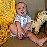baby, child, smiling, blue_outfit, couch, blanket, plush_toy, stuffed_animal, happy, indoor, cute, sitting, infant, person, cozy, knitted_blanket, foot, playful, portrait, soft_toys