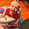 Saban is registered to the contest to win money with this photo: baby, walker, red_shirt, toy, happy, indoor, wooden_floor, kitchen, person, child, smile, blue_toy, footwear, floor, legs, infant, plastic, play, seat, expression