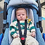 baby, infant, car_seat, seatbelt, blue, sweater, striped_clothing, pants, shoes, outdoor, sidewalk, road, toy, pacifier_clip, child, person, strapped, sitting, casual_clothing, daylight