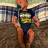 baby, infant, pacifier, onesie, clothing, blanket, pillow, bed, socks, lying_down, child, cute, indoors, soft_texture, patterned, blue, yellow_text, expression, face, person