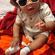 Jakhai joined the competition — help win amazing prizes! baby, child, sunglasses, hat, beige_outfit, socks, blanket, red_blanket, orange_blanket, indoor, curly_hair, pacifier, baby_clothing, cute, playful, seated, infant, portrait, person, cozy