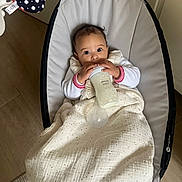 Nelya participe au concours pour gagner de l'argent avec cette photo : baby, bottle, blanket, bouncer, child, clothing, floor, furniture, indoor, milk, person, portrait, rocker, seat, soft_lighting, table, wood_floor, wide_eyes, young_child, feeding