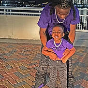 Josiah is registered to the contest to win money with this photo: adult, black_pants, brick, child, city_lights, family, fashion, happy, joy, matching_clothes, night, outdoor, pavement, person, playful, purple_shirt, railing, smile, sneakers, urban