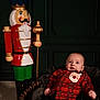 baby, child, plaid_shirt, santa_patch, basket, blanket, nutcracker, statue, toy, holiday, christmas, indoor, floor, wall_panel, smile, person, portrait, festive, decor, cozy