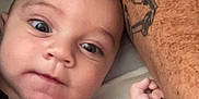Lucas is registered to the contest to win money with this photo: baby, infant, face, arm, tattoo, skin, closeup, portrait, person, expression, eyes, hand, lying_down, resting, cute, child, indoor, human, head, protection
