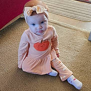 Leila is registered to the contest to win money with this photo: baby, bow, carpet, child, couch, curious_expression, cute, face, floor, furniture, headband, home, indoor, long_sleeve, pants, peach_outfit, person, rug, sitting, socks