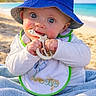 baby, beach, bib, blue_hat, bucket_hat, chewing, child, cute, giraffe, infant, ocean, outdoor, palm_tree, portrait, sand, smiling, sunny, teether, towel, wide_eyes
