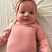 Emily is registered to the contest to win money with this photo: baby, infant, pink_clothing, headband, bow, smile, face, lying_down, soft_fabric, child, cute, portrait, closeup, indoor, person, newborn, headwear, skin, eyes, young