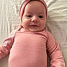 baby, infant, pink_clothing, headband, bow, smile, face, lying_down, soft_fabric, child, cute, portrait, closeup, indoor, person, newborn, headwear, skin, eyes, young
