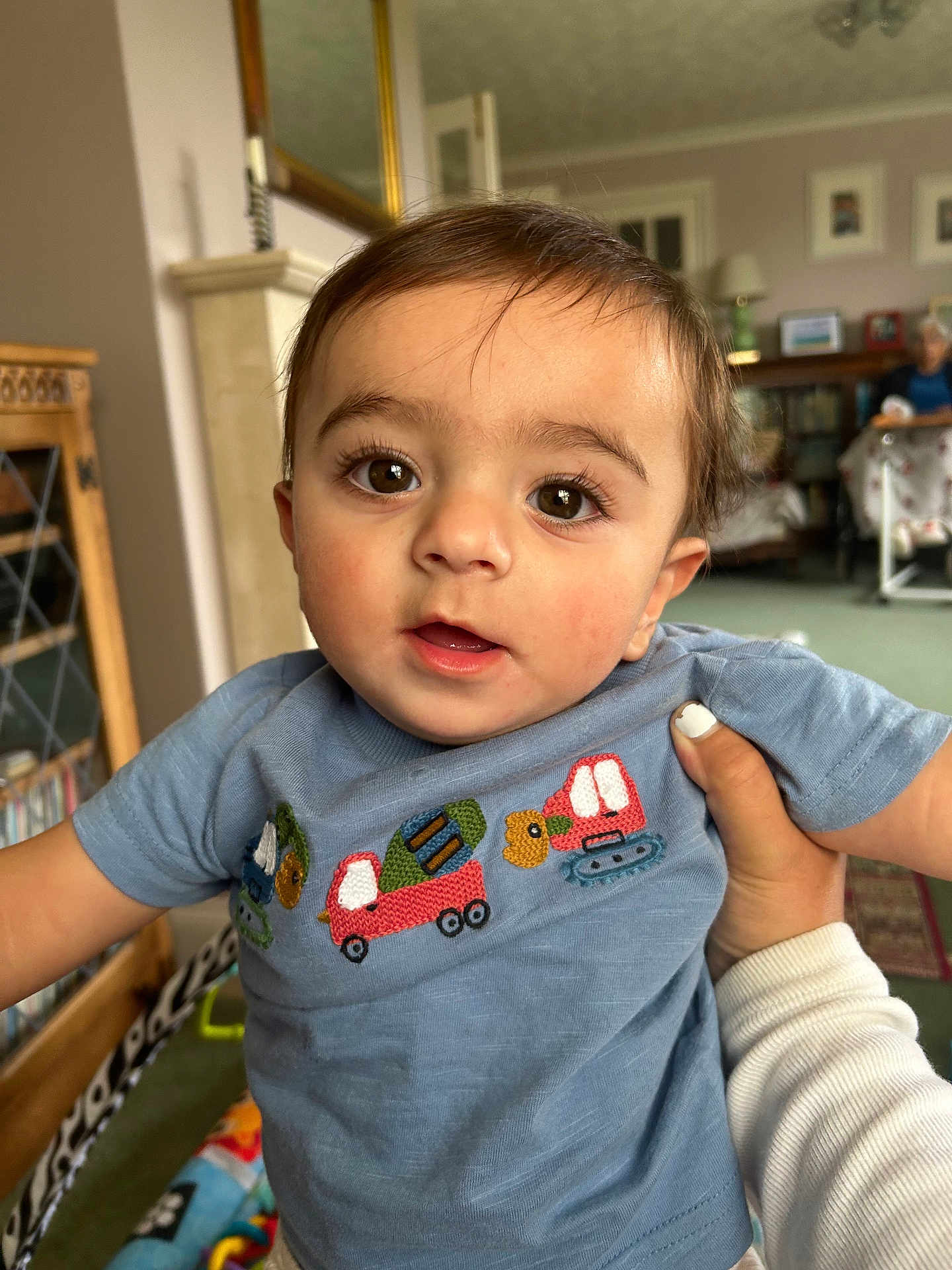 Kyh is registered to the contest to win money with this photo: toddler, child, face, eyes, blue_shirt, embroidery, hand, nail_polish, living_room, furniture, person, indoors, curious, portrait, closeup, carpet, mirror, bookshelf, elderly_person, cozy