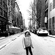 Kaitlyn is registered to the contest to win money with this photo: child, hoodie, street, urban, city, sidewalk, car, building, tree, black_and_white, smile, casual_clothing, empty_street, young_person, hood, sneakers, outdoor, daytime, pose, road
