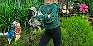 Kaitlyn joined the competition — help win amazing prizes! child, girl, green_sweater, black_pants, white_shoes, garden, plants, tree, statues, figurines, smile, pigtails, fence, outdoor, nature, gravel, playful, confident, portrait, casual_clothing