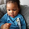 Messiah is registered to the contest to win money with this photo: baby, infant, child, portrait, curly_hair, blue_clothing, sitting, car_seat, seatbelt, face, eyes, lips, serious_expression, indoor, couch, close_up, photography, fist, safe, adorable