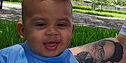 Zayden is registered to the contest to win money with this photo: baby, child, smiling, blue_shirt, nike, grass, outdoor, tattoo, arm, blanket, park, trees, sitting, happy, person, playful, sunny, daytime, face, clothing