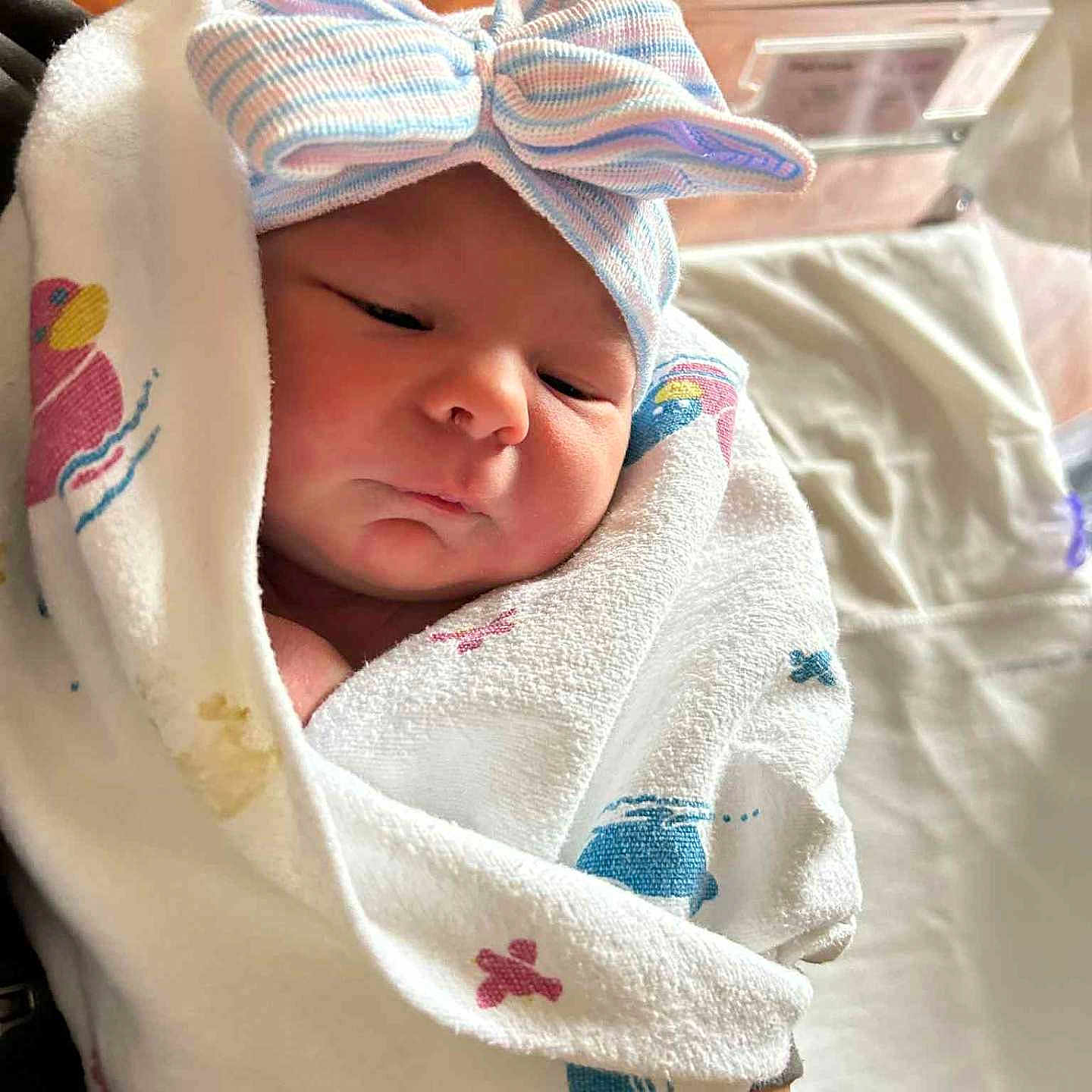 Vayda is registered to the contest to win money with this photo: baby, blanket, bow, closeup, cute, face, hat, hospital, indoor, infant, newborn, peaceful, person, resting, sleepy, striped, towel, wood_floor, wrapped, wristband
