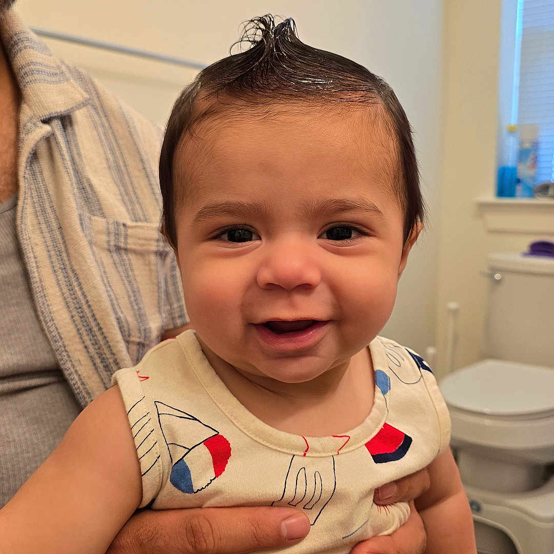 Matteo is registered to the contest to win money with this photo: baby, child, infant, smiling, portrait, indoor, bathroom, adult, parent, holding, hair, spiky_hair, eyes, face, onesie, colorful_clothing, toilet, window, happy, photography