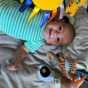 David participe au concours pour gagner de l'argent avec cette photo : baby, infant, striped_onesie, play_mat, plush_toys, stuffed_animal, smiling, happy, child, indoor, floor, colorful, toy_rings, soft_surface, lying_down, cute, young_child, playtime, baby_toys, joyful