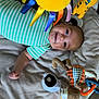 baby, infant, striped_onesie, play_mat, plush_toys, stuffed_animal, smiling, happy, child, indoor, floor, colorful, toy_rings, soft_surface, lying_down, cute, young_child, playtime, baby_toys, joyful