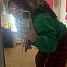 Pepper is registered to the contest to win money with this photo: cat, person, mirror, selfie, glasses, green_sweatshirt, red_pajama_pants, carpet, room, pink_wall_hanging, furniture, decor, phone, long_hair, playing, indoor, pet, casual, fun, reflection