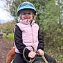 child, helmet, pony, horseback_riding, outdoor, smile, vest, reins, nature, trail, autumn, greenery, happy, person, animal, animal_riding, young_child, casual_clothing, daytime, forest