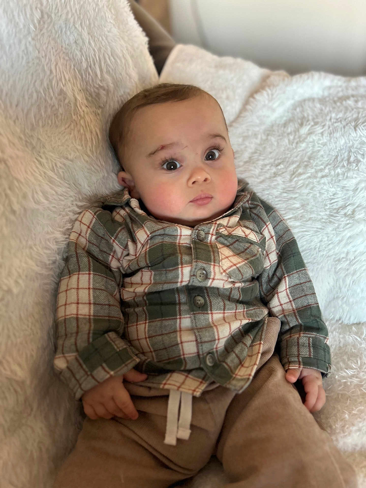 George joined the competition — help win amazing prizes! baby, infant, plaid_shirt, pants, blanket, soft_texture, curious_expression, indoor, child, cute, portrait, seated, cozy, buttoned_shirt, hands, face, eyes, head, young_child, casual_clothing
