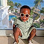 toddler, child, sunglasses, romper, shoes, indoor, glass_window, sea, palm_trees, sunlight, smiling, fashion, pose, floor, resort, vacation, outdoor_view, shadow, happy, portrait